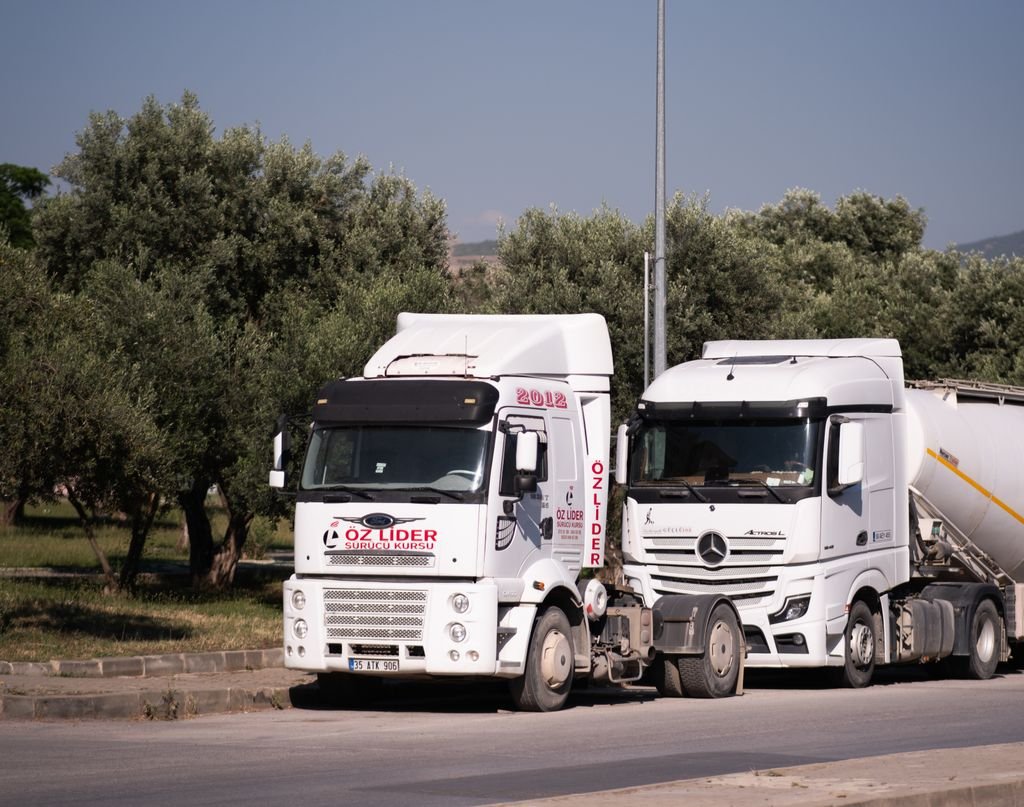 Two trucks parked on a road near olive trees in İzmir, Türkiye.